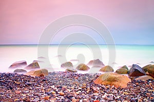 Romantic atmosphere in peaceful morning at sea. Big boulders sticking out from smooth wavy sea. Pink horizon