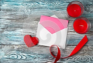 Romantic background with envelope, heart, candles and ribbon on a wooden gray-blue background.