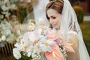 Romantic and beautiful woman in white wedding dress holding a big fresh bouquet of pink and white flowers in her hands