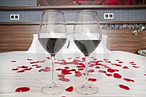 Romantic bedroom - glasses of red wine and rose petals on a bed