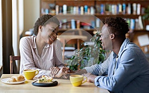 Romantic black couple having breakfast together at cafe, holding hands and looking at each other, panorama