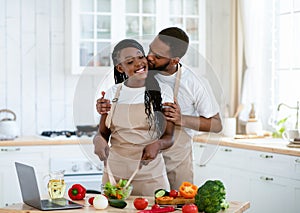 Romantic Black Couple Kissing While Cooking Healthy Food Together In Kitchen