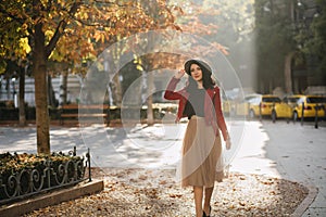 Romantic black-haired girl in long lush skirt enjoying sunshine in autumn park. Outdoor portrait of shy brunette female