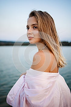 Romantic blonde woman in pink robe on the beach by the sea at sunset.