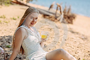 Romantic blonde woman in straw hat having picnic on sea beach. Fresh fruits, juice, cookies and peaches