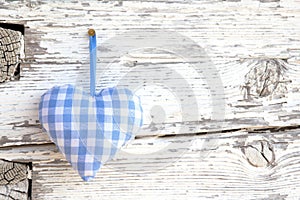 Romantic blue/white checkered heart shape hanging above white wooden surface on a nail- white wooden shabby chic background for