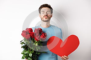 Romantic boyfriend waiting for kiss, holding bouquet of roses flowers and big red heart on Valentines day, love in air