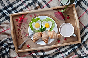 Romantic breakfast in bed with heart-shaped eggs, jam toasts, croissants, rose flower and petals