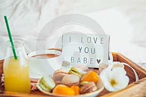 Romantic Breakfast in bed with I love you baby text on lighted box. Cup of coffee, juice, macaroons, flower and gift box on wooden