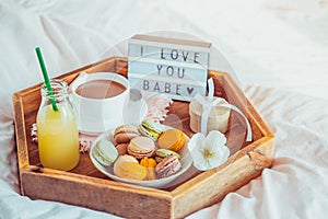 Romantic Breakfast in bed with I love you baby text on lighted box. Cup of coffee, juice, macaroons, flower and gift box on wooden