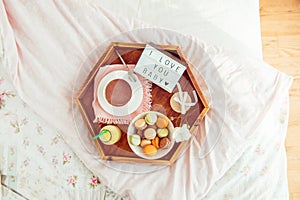 Romantic Breakfast in bed with I love you baby text on lighted box. Cup of coffee, juice, macaroons, flower and gift box on wooden