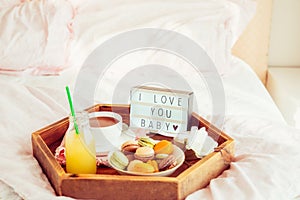 Romantic Breakfast in bed with I love you baby text on lighted box. Cup of coffee, juice, macaroons, flower and gift box on wooden