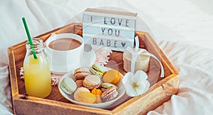 Romantic Breakfast in bed with I love you baby text on lighted box. Cup of coffee, juice, macaroons, flower and gift box on wooden