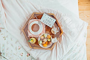 Romantic Breakfast in bed with I love you baby text on lighted box. Cup of coffee, juice, macaroons, flower and gift box on wooden