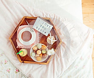 Romantic Breakfast in bed with I love you baby text on lighted box. Cup of coffee, juice, macaroons, flower and gift box on wooden