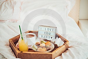 Romantic Breakfast in bed with I love you baby text on lighted box. Cup of coffee, juice, macaroons, flower and gift box on wooden