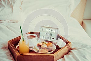 Romantic Breakfast in bed with I love you baby text on lighted box. Cup of coffee, juice, macaroons, flower and gift box on wooden