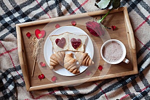 Romantic breakfast in bed for Valentines Day. Toasts with jam, croissants, hot chocolate, red rose flower and petals