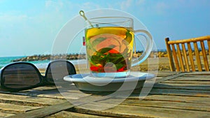 Romantic breakfast in a cafÃ© on the beach. Sunglasses and black tea with mint in a cup on a wooden table