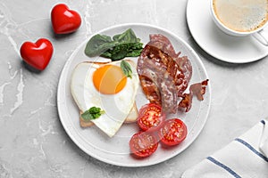 Romantic breakfast with fried bacon and heart shaped egg on grey table, flat lay. Valentine`s day celebration