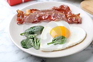 Romantic breakfast with fried bacon and heart shaped egg on white marble table, closeup. Valentine`s day celebration