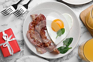 Romantic breakfast with fried bacon and heart shaped egg on white marble table, flat lay. Valentine`s day celebration