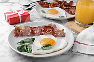 Romantic breakfast with fried bacon and heart shaped egg on white marble table. Valentine`s day celebration