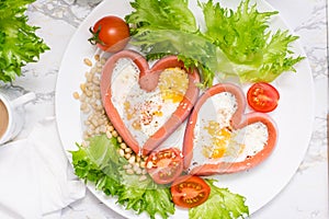 Romantic breakfast. Fried eggs in heart shaped sausages, lettuce and cherry tomatoes on a plate on the table. Top view. Close-up