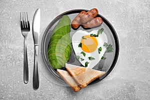 Romantic breakfast with fried heart shaped egg, avocado, sausages and toasts on light grey table, flat lay. Valentine`s day