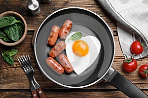 Romantic breakfast with fried sausages and heart shaped egg on wooden table, flat lay. Valentine`s day celebration