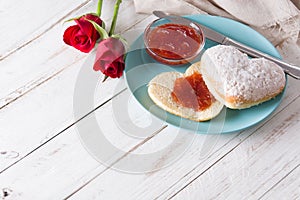 Romantic breakfast heart-shaped bun and berry jam and roses on white wooden table