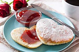 Romantic breakfast with heart-shaped bun and berry jam on white wooden table.