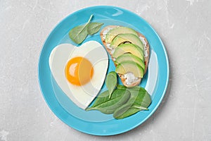 Romantic breakfast with heart shaped fried egg on light grey table, top view