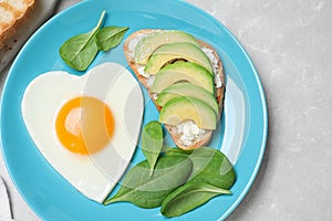 Romantic breakfast with heart shaped fried egg on light grey table, top view