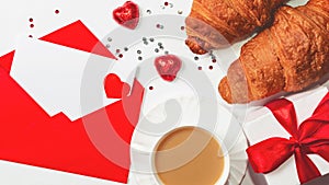 A romantic breakfast for a loved one on Valentine`s Day. Fresh delicious croissants with a cup of coffee, chocolate hearts, paper