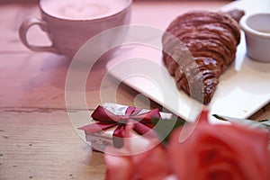 Romantic breakfast for Valentine`s Day celebrate. Present box, rose flowers, fresh croissant coffee on wooden table. Focus at box