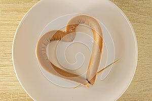 Romantic Breakfast on Valentine`s Day: sausage in the shape of a heart, pierced with a toothpick on the plate. Menu for Valentine