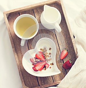 Romantic breakfast . Yogurt with granola and strawberry in bow
