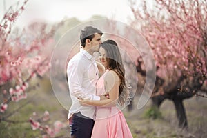 Romantic bridegroom kissing bride on forehead while standing against wall covered with pink flowers
