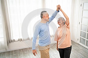 Romantic and cheerful Asian well-being senior couple enjoy dancing and holding hands to music together with smiles and happiness