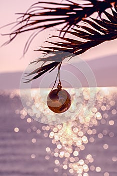 Romantic Christmas background. Palm tree with Christmas ball, blurred sea and bokeh. Christmas greeting card. Vertical