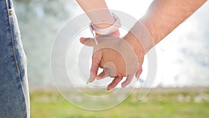 Romantic closeup of a young man`s hand holding a young woman`s hand when the happy couple is standing in the park near