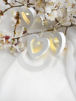 Romantic composition with blooming cherry branch, heart lights on white silk background. Elegant greeting concept