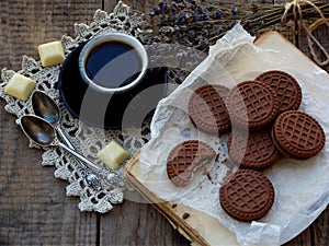 Romantic composition of chocolate cookies with white cream, cup of coffee and bouquet lavender on wooden background. Selective foc