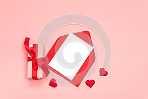 Romantic composition with surprise gift box, red ribbon bow, red envelope with paper on a pink background. Holiday wish list