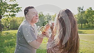A romantic couple blowing a bunch of dandelions in the summer in a meadow in the sun. Happy together.