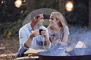 Romantic Couple Camping Sitting By Bonfire In Fire Bowl With Hot Drinks