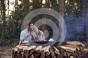 Romantic Couple Camping Sitting By Bonfire In Fire Bowl With Hot Drinks