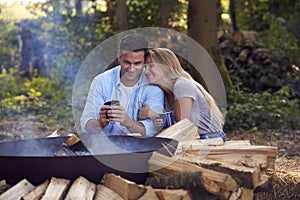 Romantic Couple Camping Sitting By Bonfire In Fire Bowl With Hot Drinks