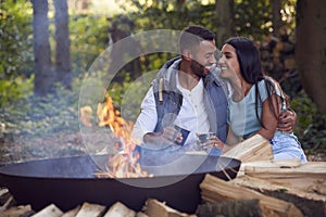 Romantic Couple Camping Sitting By Bonfire In Fire Bowl With Hot Drinks